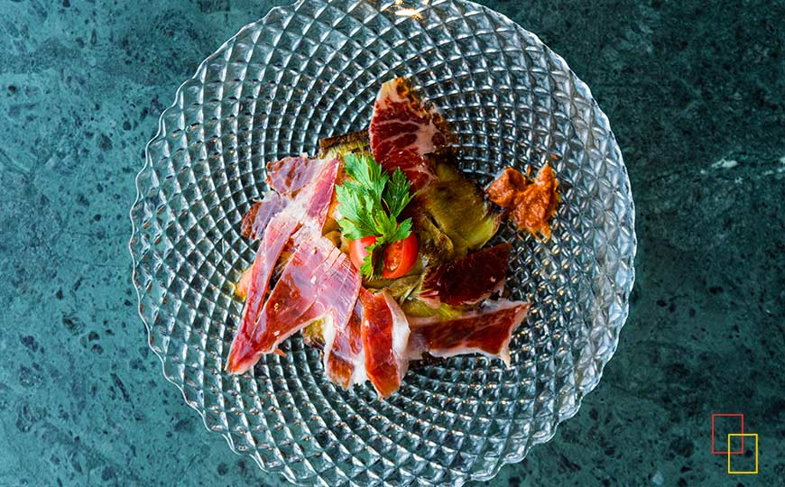 Alcachofa confitada con jamón ibérico de bellota y romescu