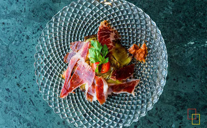 Alcachofa confitada con jamón ibérico de bellota y romescu