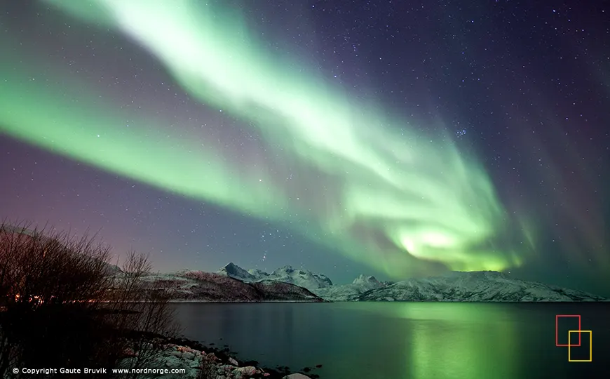 Auroras boreales sobre fiordo y montañas cerca de Tromsø