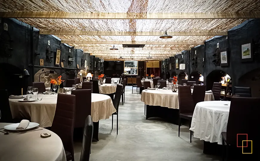 Sala principal del restaurante brasería La Bodega con mesas redondas y paredes de piedra