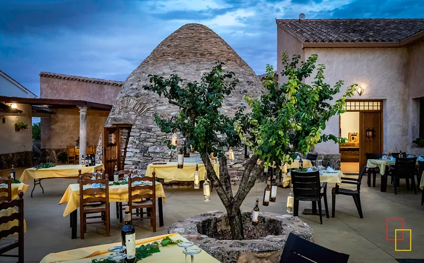 Patio de Bodega Las Calzadas al atardecer con cubo de piedra y mesas preparadas