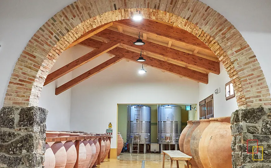 Sala de tinajas de barro con arcos de piedra y techos de madera en Bodega Las Calzadas