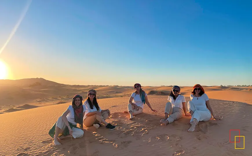 Grupo de viajeras sentadas en las dunas del Sahara al atardecer