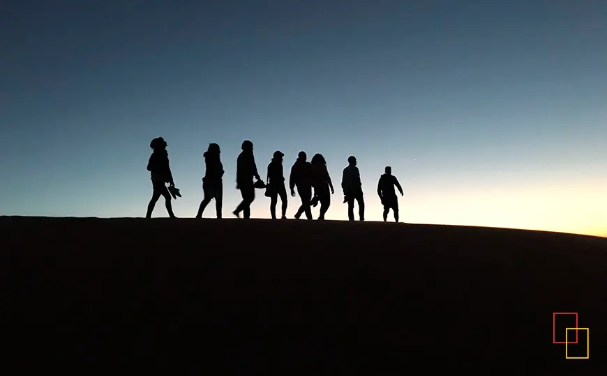 Siluetas caminando sobre la cresta de una duna al atardecer