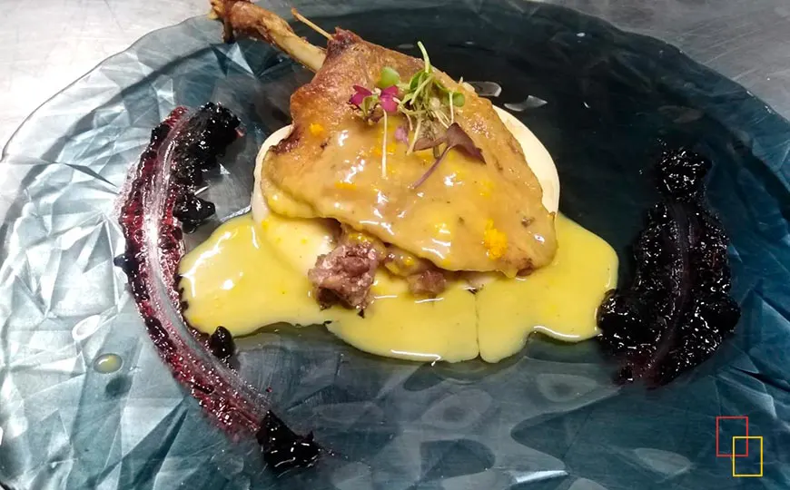 Muslo de pato confitado sobre crema de patata, frutos rojos y salsa de naranja