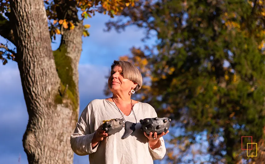 Artesana letona sosteniendo piezas de barro negro junto a un árbol