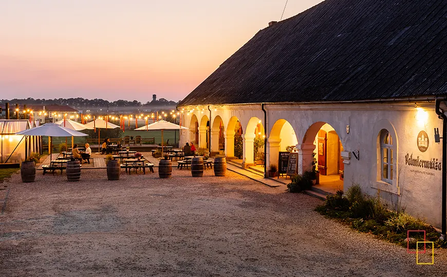 Terraza de la cervecería Valmiermuiža al atardecer con luces y mesas al aire libre