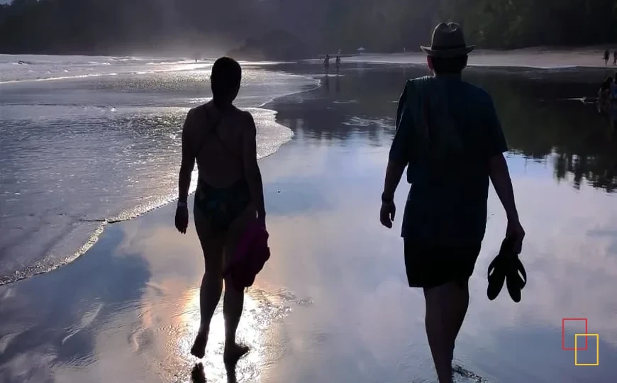 Dos personas caminando por una playa de Costa Rica con reflejos del sol en la arena mojada
